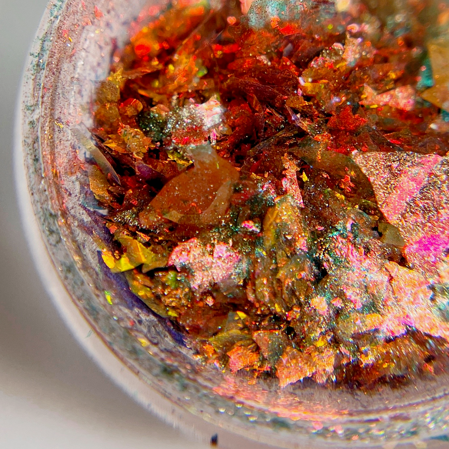 A close-up view of a collection of multi-colored coral quartz nail flakes inside a clear container, showcasing various shades such as blue, orange, and red.