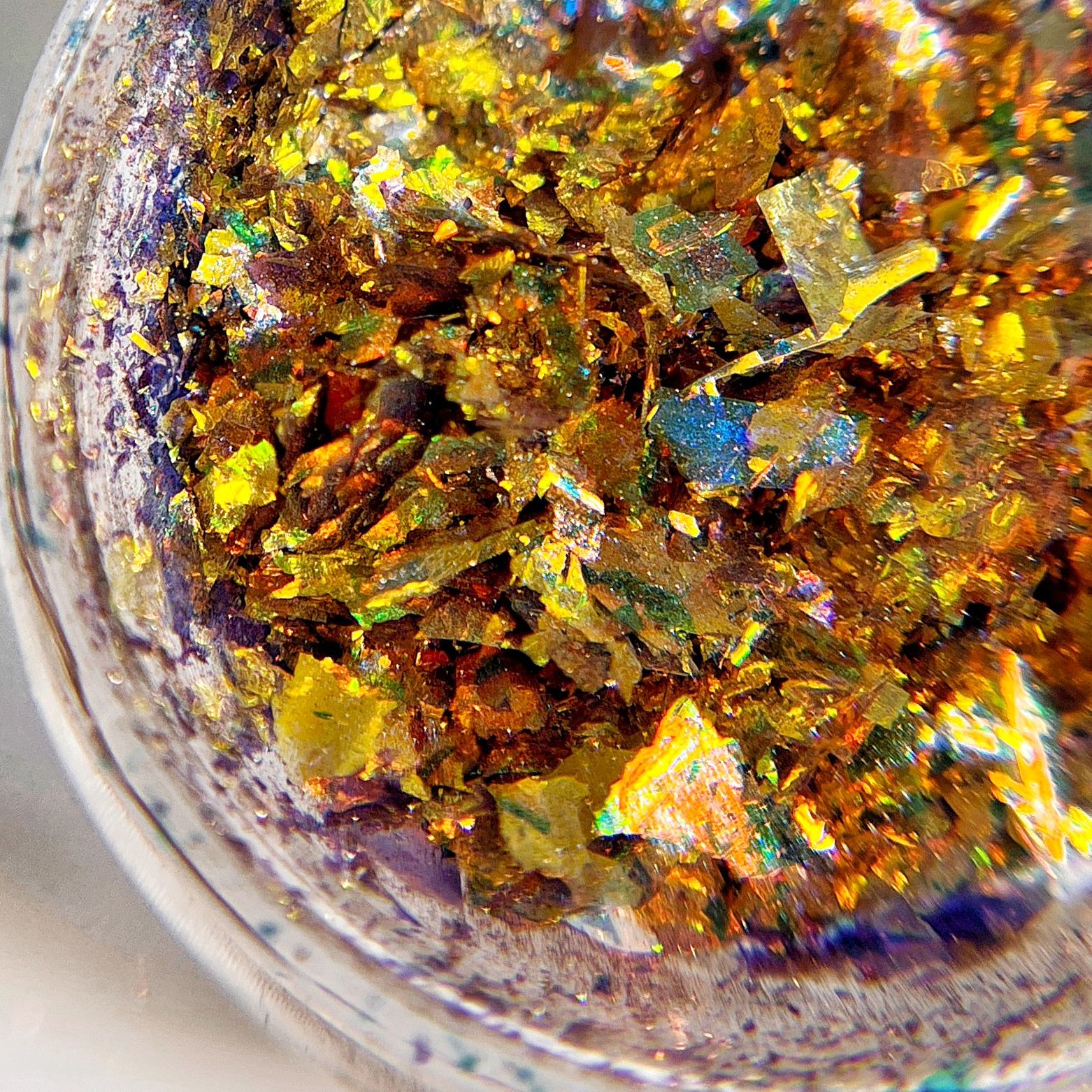 Close up of iridescent flakes in transparent jar on white background.