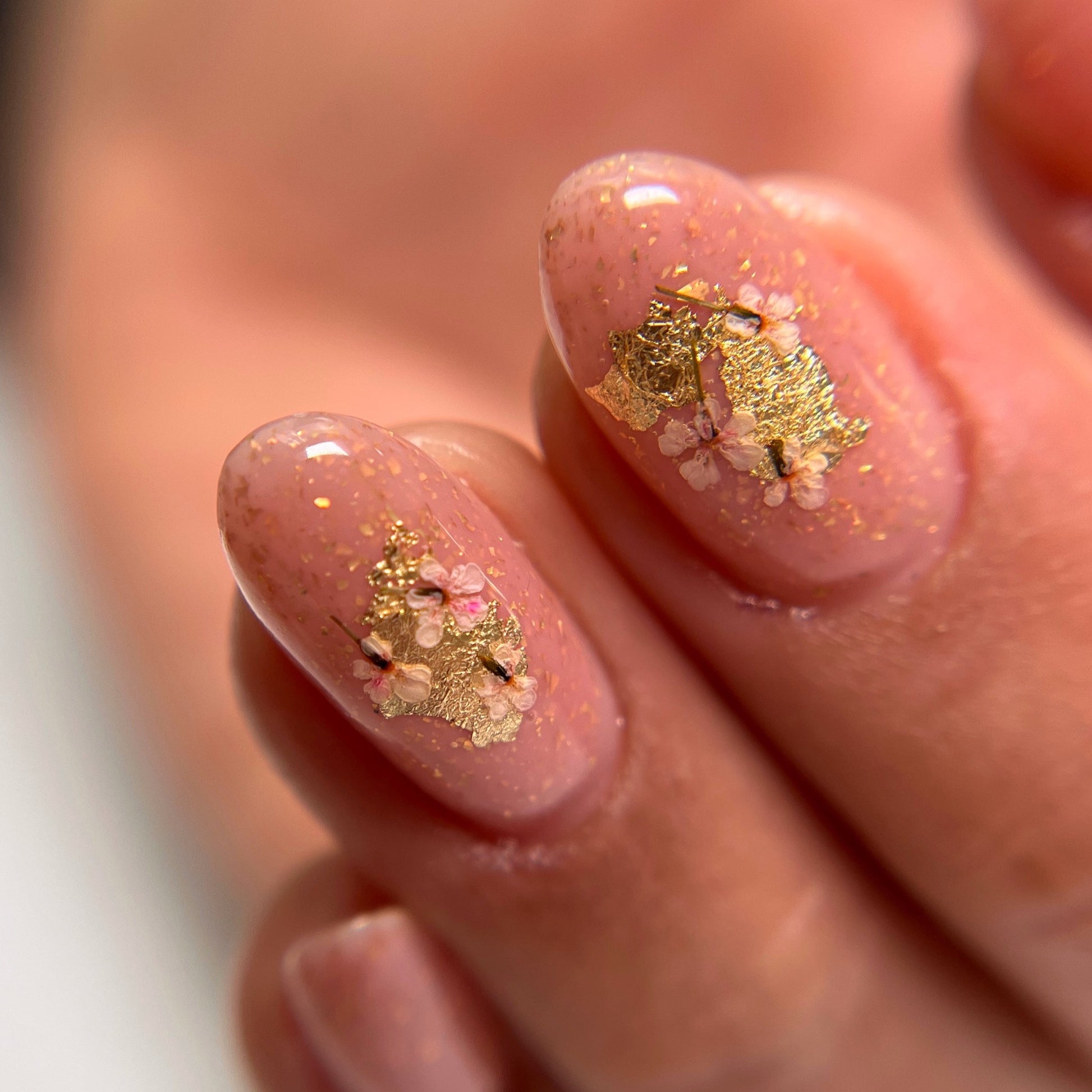 A nail art example featuring gold foil leaf and encapsulated flowers. 
