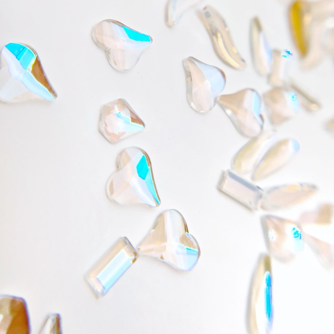 Multi shape iridescrnt rhinestones scattered on a white background. 
