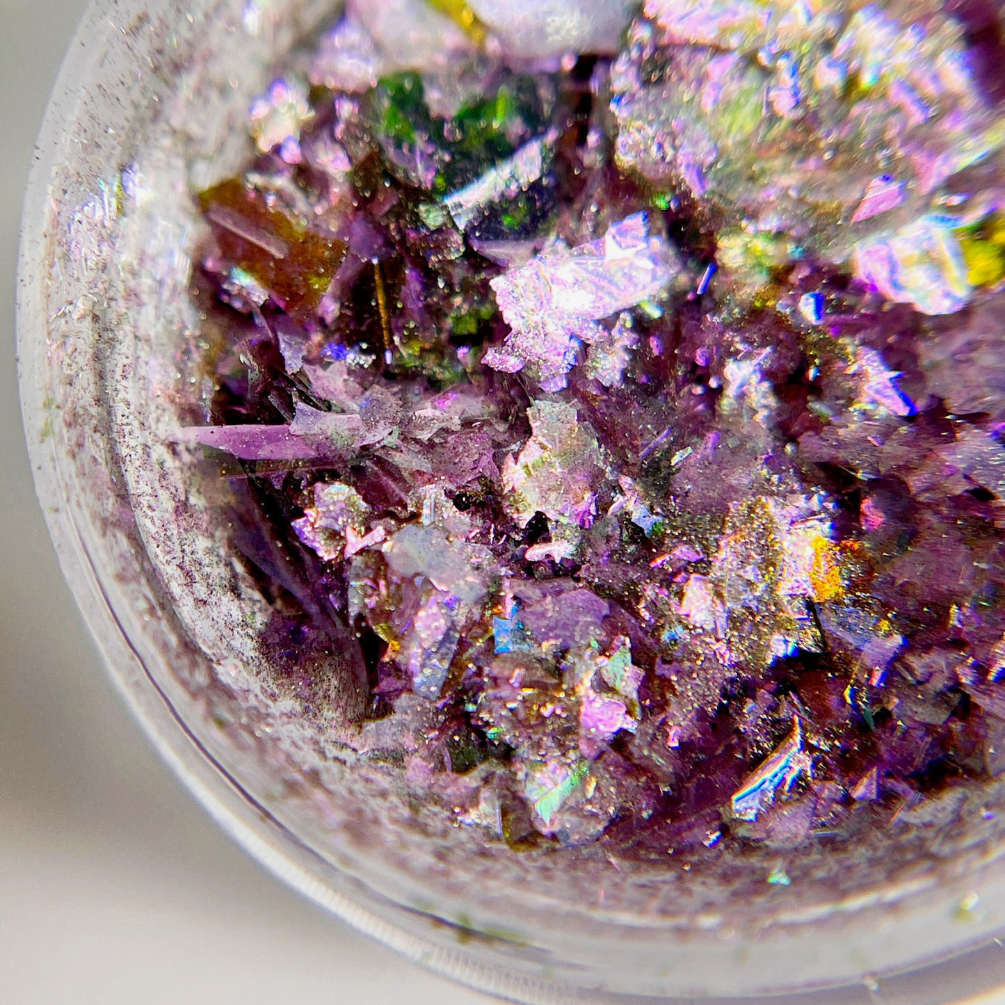 Close up of purple multicolor iridescent flakes in transparent jar on white background.